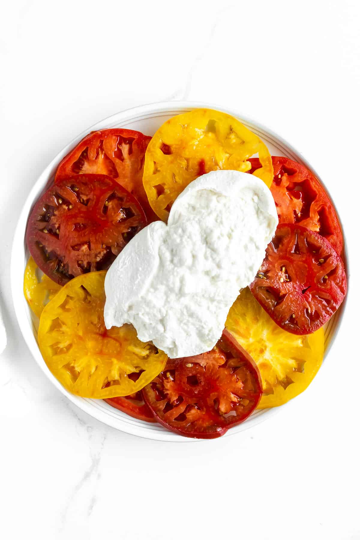 Sliced tomatoes on platter topped with burrata.
