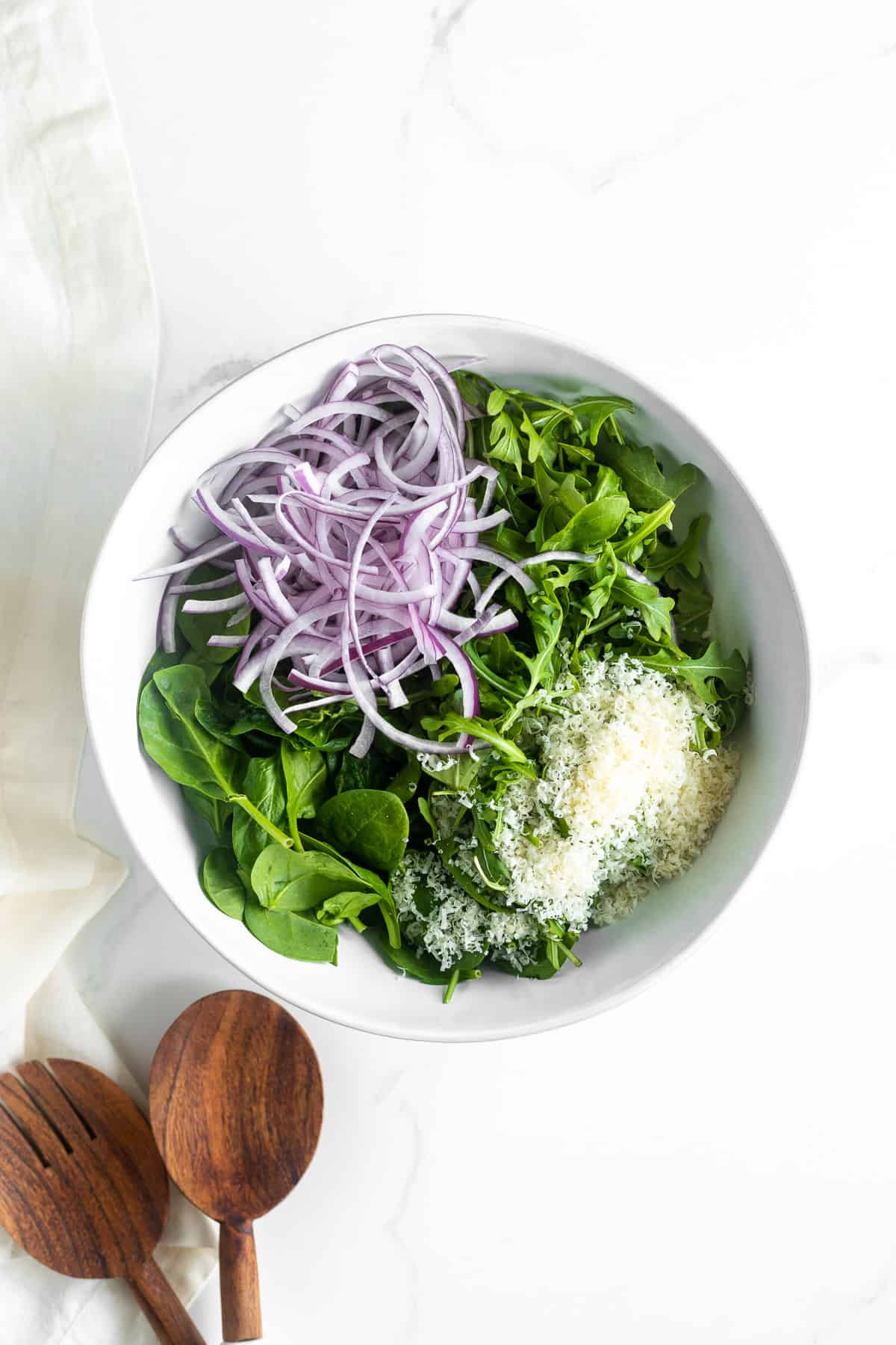 Greens in a bowl with sliced red onion and parmesan.