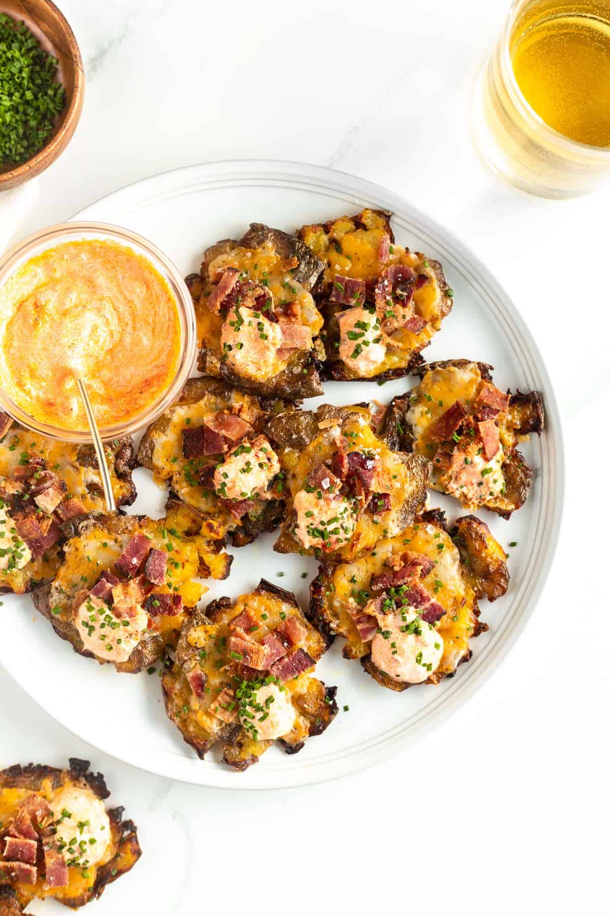 Cheesy smashed potatoes on a plate topped with bacon and chives.